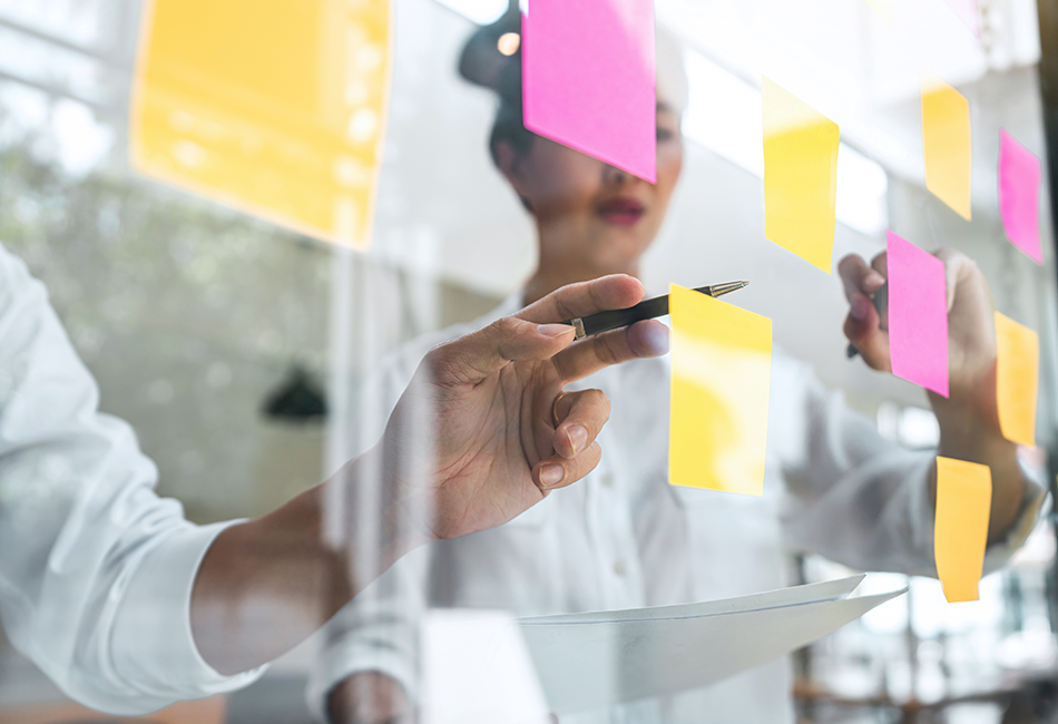 950x650 - A man pointing at a clear board with sticky notes on it