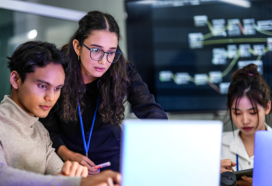 950x650 - Two people on a laptop and someone in the background on their phone